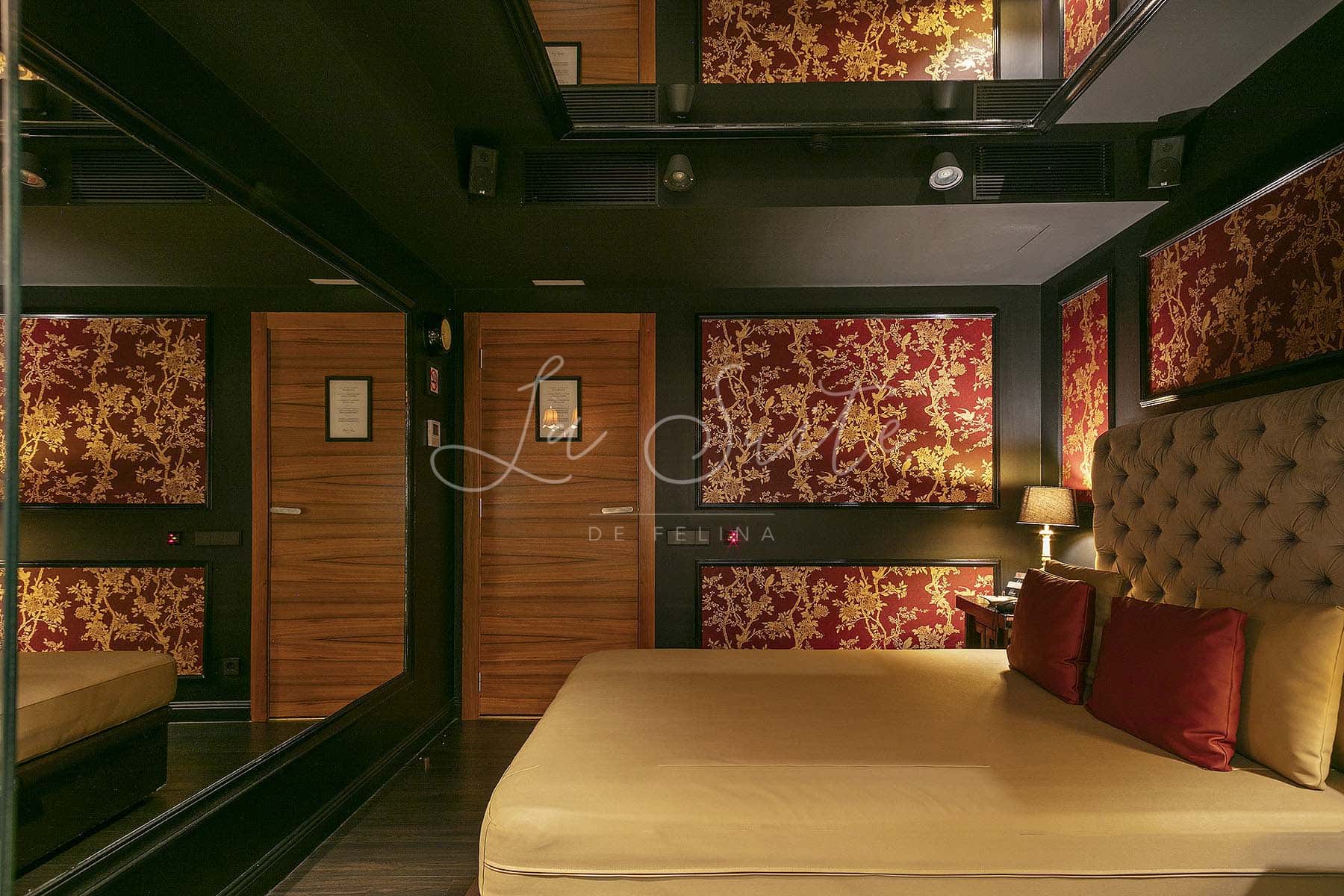 Chambre de luxe aux murs rouges et à la décoration dorée dans la maison close La Suite Barcelona